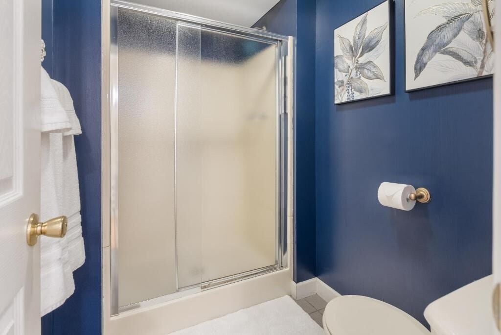 Un baño con mampara de vidrio, inodoro e ilustraciones botánicas enmarcadas en la pared.