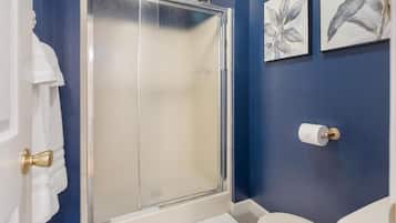Un baño con mampara de vidrio, inodoro e ilustraciones botánicas enmarcadas en la pared.