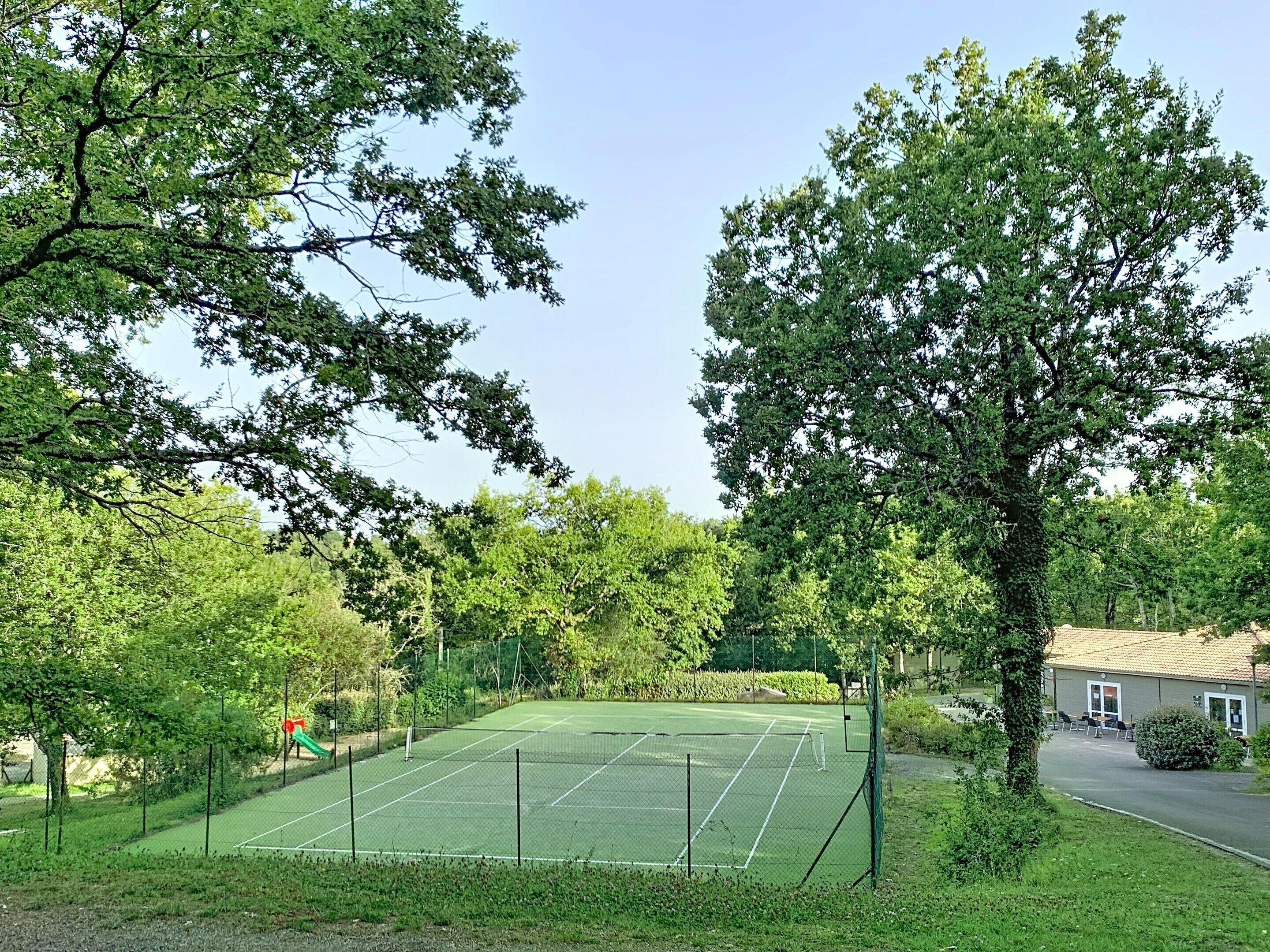 A tennis court surrounded by trees, with a building in the background.