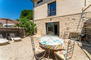 Un bâtiment en pierre doté d’un patio comprenant une table et des chaises, une clôture en bois et un barbecue.