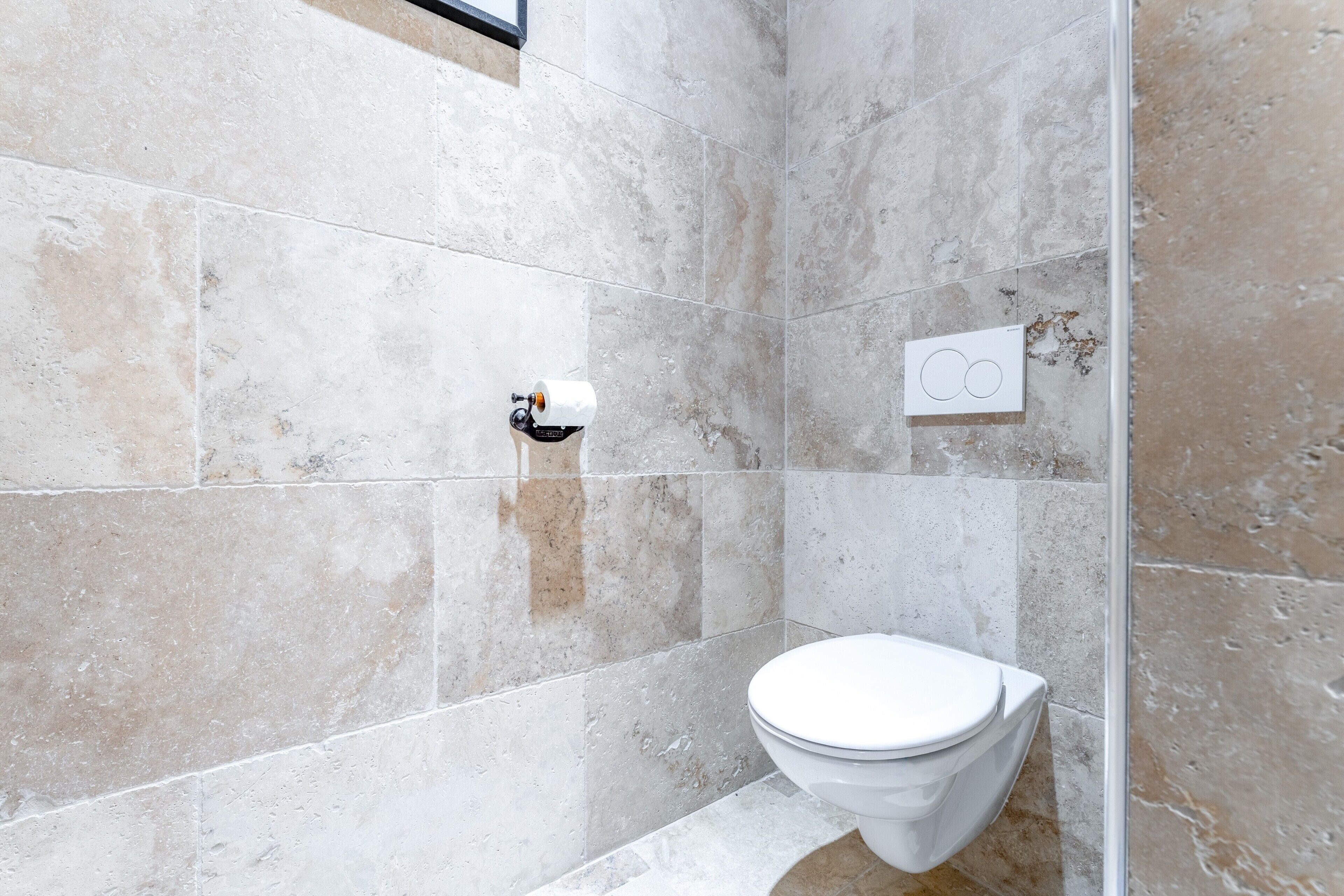 A bathroom with a toilet, a paper towel dispenser, and a wall-mounted control panel.