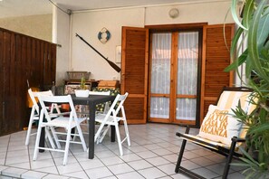 A patio with a table and chairs, a wooden door, and a bench with a cushion. - M450 - Marcelli, two-room apartment with patio (Marcelli)