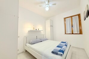 A bedroom with a bed, a ceiling fan, a wardrobe, and a window with curtains. - M450 - Marcelli, two-room apartment with patio (Marcelli)