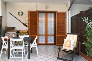 A patio with a table and chairs, a wooden door, and a plant. - M450 - Marcelli, two-room apartment with patio (Marcelli)