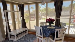 A dining area with a table set for four, a bench, and a view through large windows. - “Ocean Breeze” 1BDR, 1Bath cottage on Nettles Island, close to beach and river (Jensen Beach)