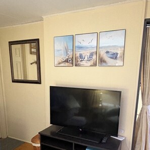 A living room with a flat-screen TV on a stand, a door with a mirror, and three beach-themed paintings on the wall.