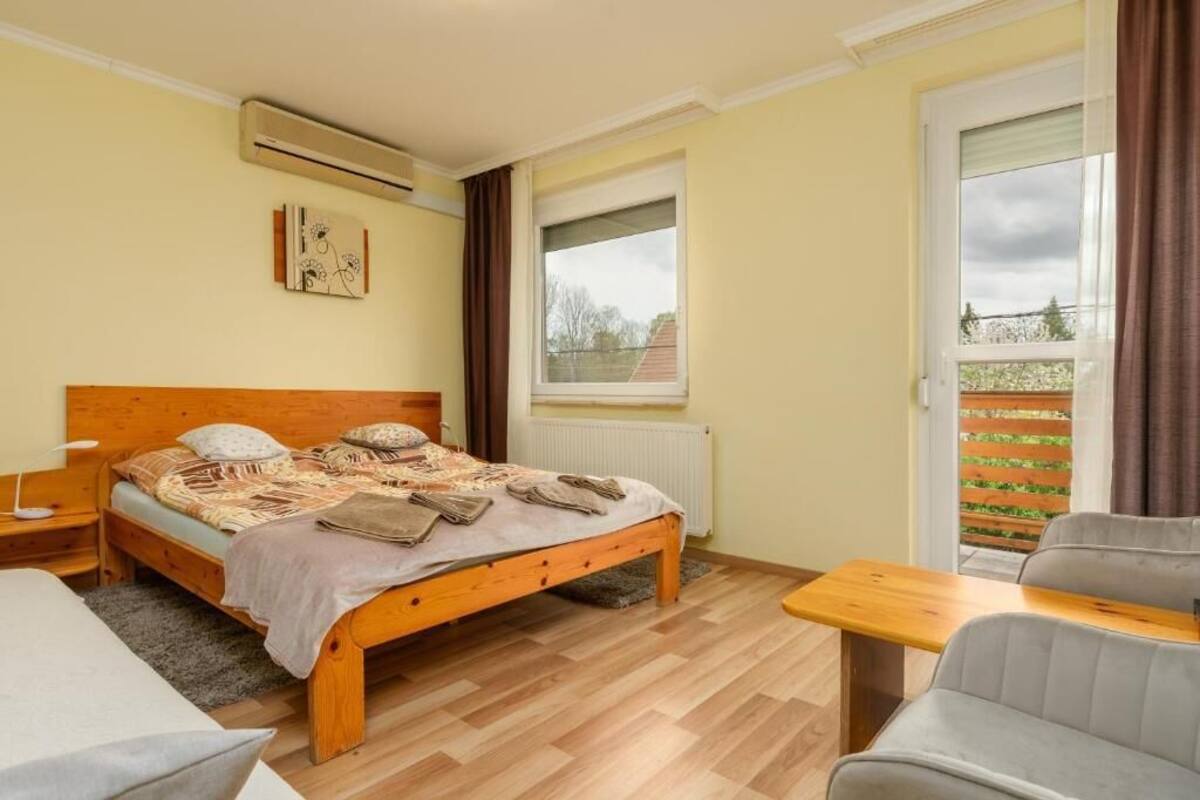 Un dormitorio con una cama de madera, una mesita pequeña, una silla, una ventana y un equipo de aire acondicionado.