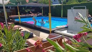 Zona de piscina exterior con sombrillas, mobiliario junto a la piscina y una fuente de agua.