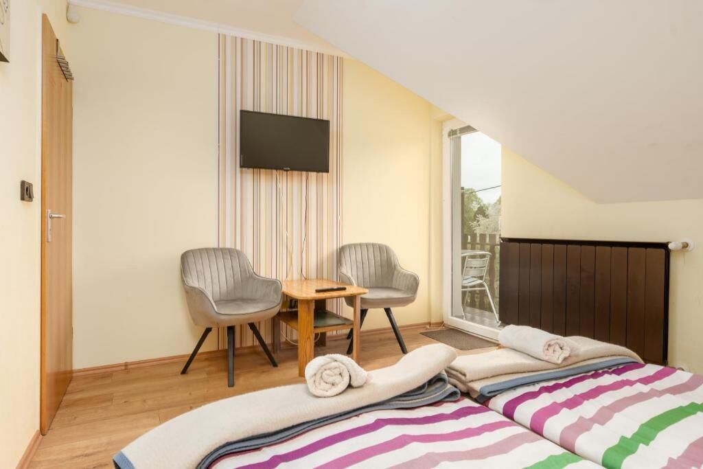 A bedroom with a bed, two chairs, a TV, and a window.