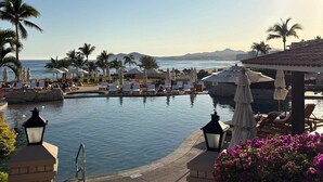 En pool vid semesteranläggningen, med solstolar, palmer och utsikt över havet.
