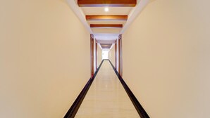A long, narrow hallway with a polished floor and wooden beams on the ceiling. - Deluxeabirami Grand Inn (Kodaikanal)