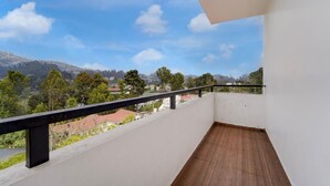 A balcony with a wooden floor and a black railing, overlooking a residential area with trees and houses under a clear blue sky. - Deluxeabirami Grand Inn (Kodaikanal)