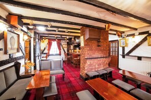 A pub interior with wooden tables and benches, a red carpet, and exposed brick walls. - Royal Hotel (Gateshead)