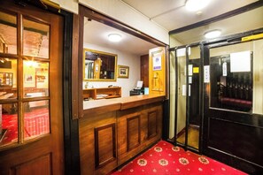 A reception area with a wooden counter, a mirror, and a red carpeted floor. - Royal Hotel (Gateshead)