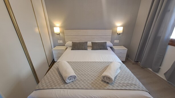 A hotel room with a large bed, two bedside tables, a headboard, and two wall-mounted lamps.