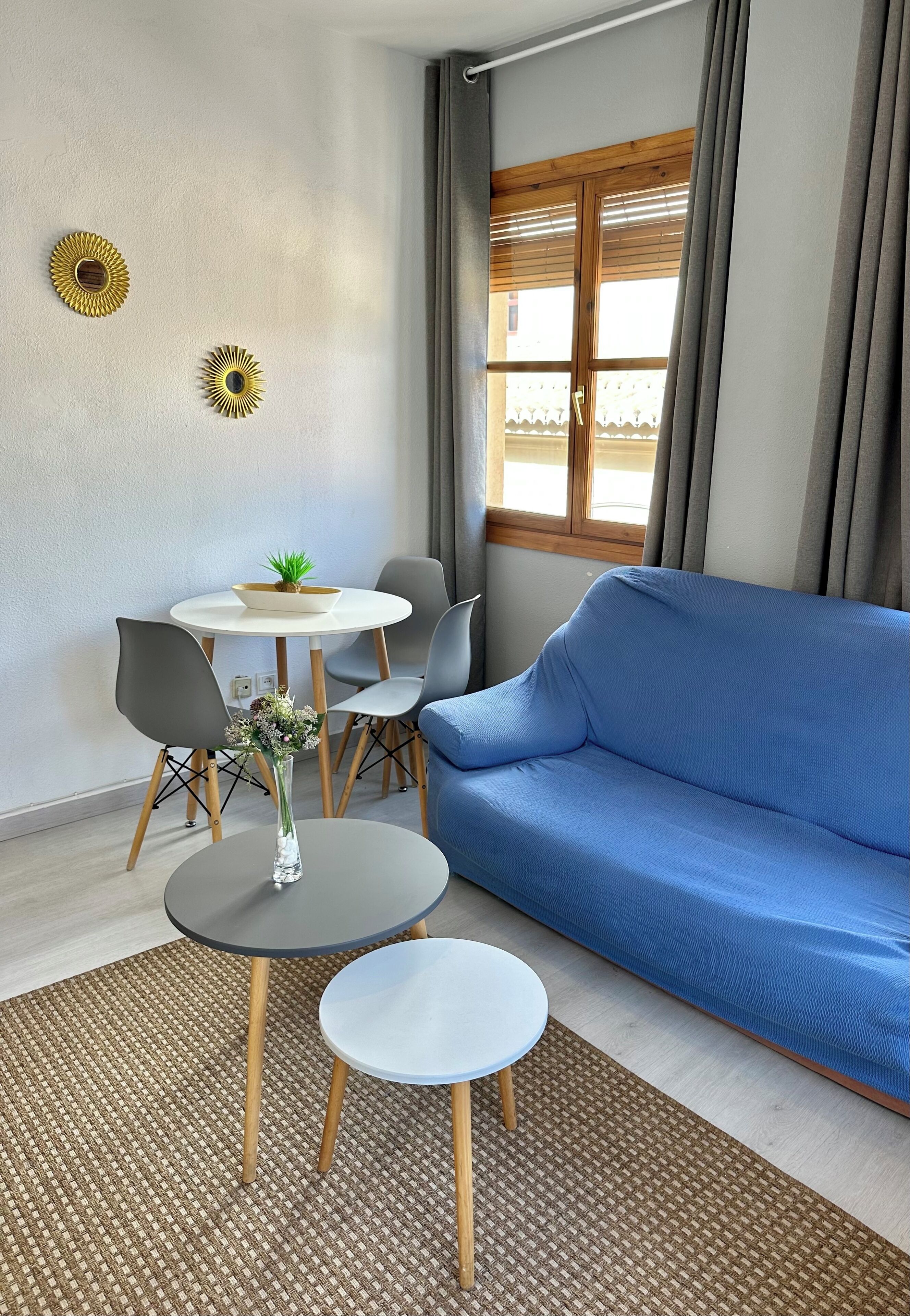 Una sala moderna con un sofá azul, una mesa de comedor redonda con sillas, una mesita auxiliar y dos adornos de pared.