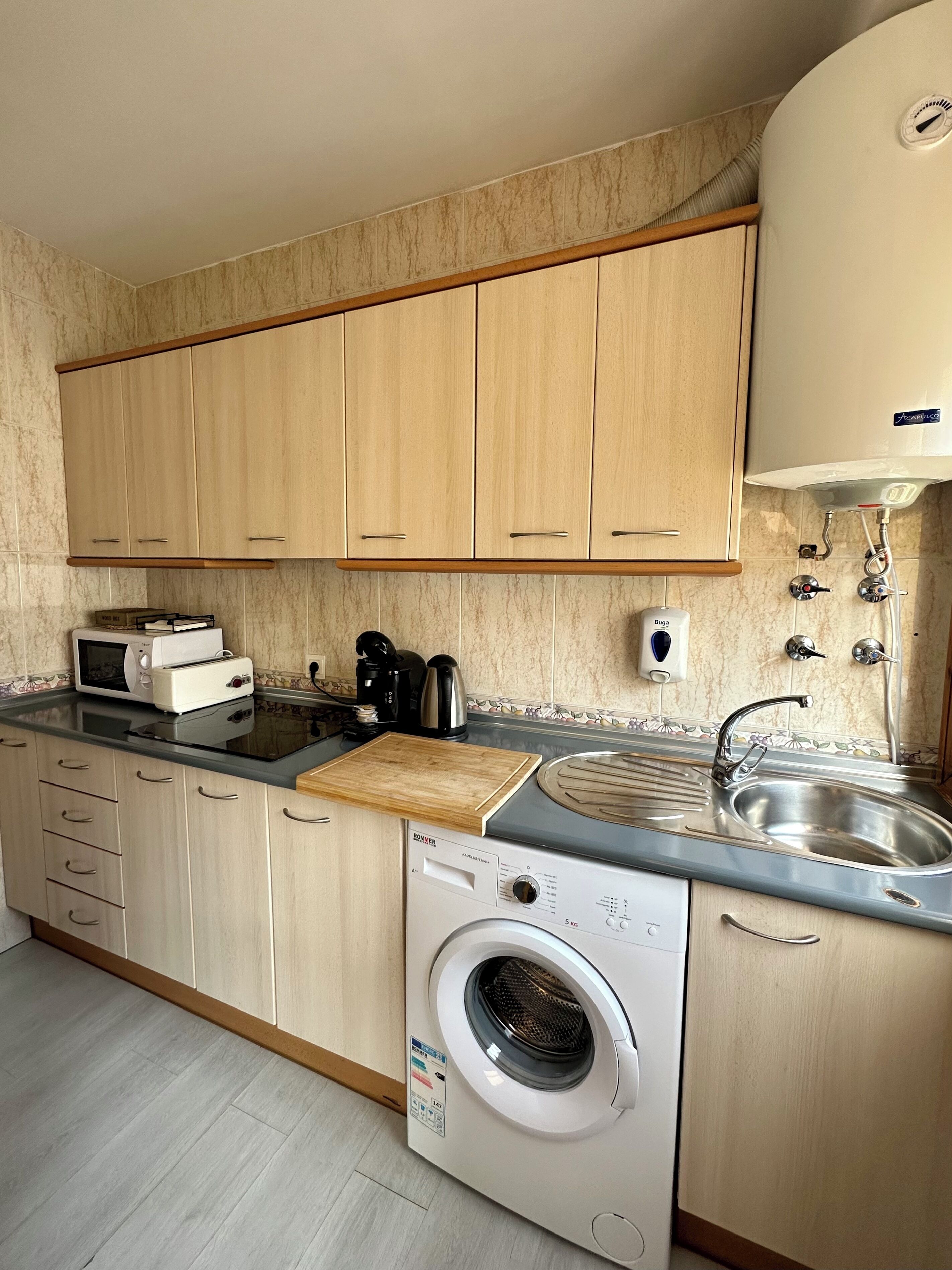 Une cuisine compacte avec des meubles en bois, un lave-linge encastré, un four à micro-ondes et un évier.