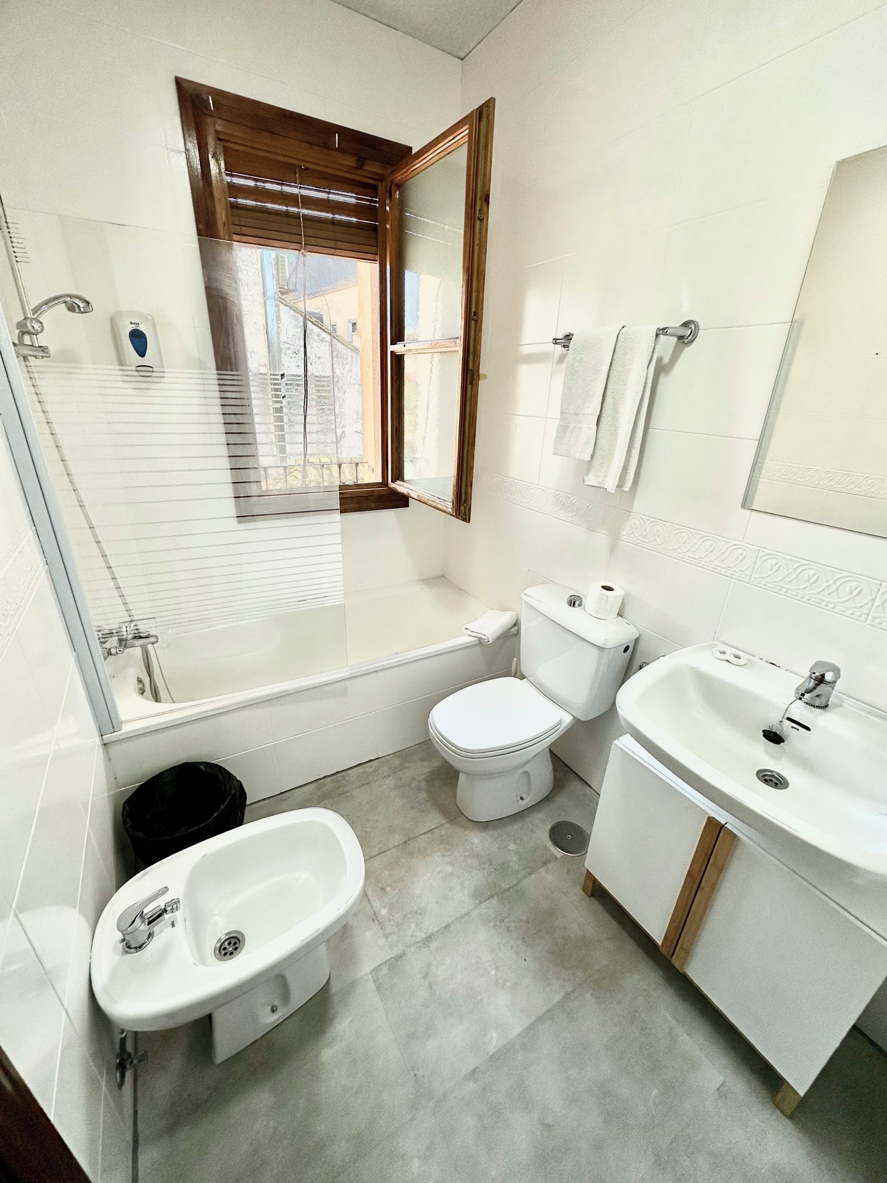 Un baño con bañera, inodoro, lavamanos y una ventana con persianas.