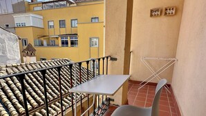 A balcony with a table and chair, a metal railing, and a view of yellow buildings.