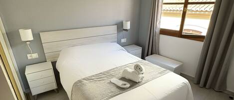 Une chambre à coucher bien rangée, avec un lit, des tables de chevet, une lampe et une fenêtre avec des rideaux.