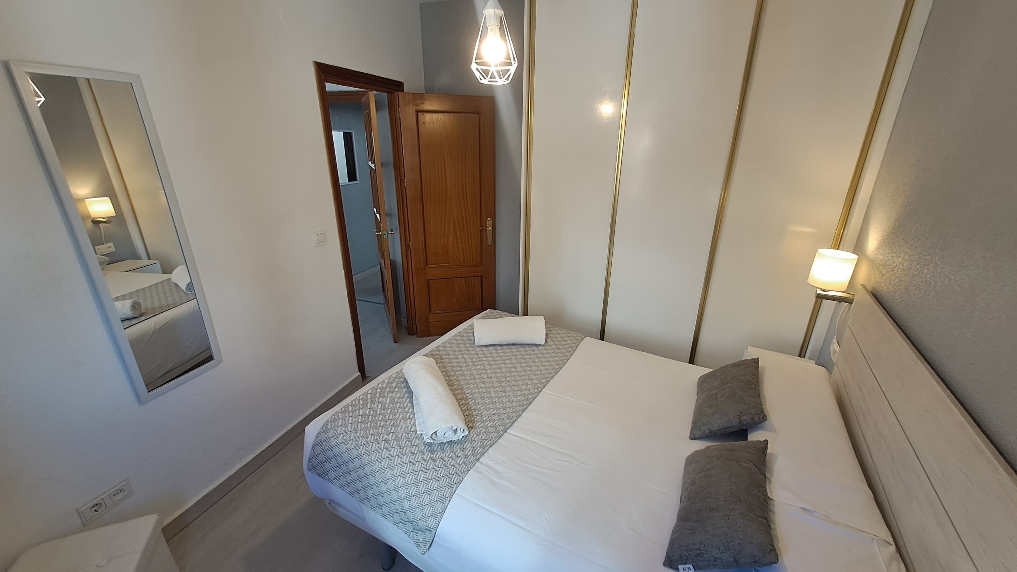 A hotel room with a bed, a mirror, a door, and a light fixture.