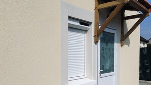 A building with a white exterior, a wooden door, a window with a shutter, and a small step leading to the entrance. - 1-bedroom house 8 minutes from the 24H circuit (Allonnes)