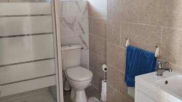 A bathroom with a shower, toilet, sink, and a window.