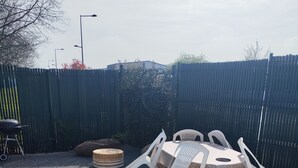 An outdoor seating area with a round table and chairs, a barbecue grill, and two planters with small plants. - 1-bedroom house 8 minutes from the 24H circuit (Allonnes)