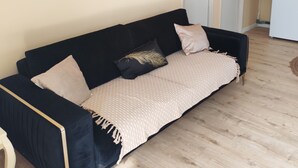 A room with a black sofa, beige walls, a clock, and a white refrigerator. - 1-bedroom house 8 minutes from the 24H circuit (Allonnes)