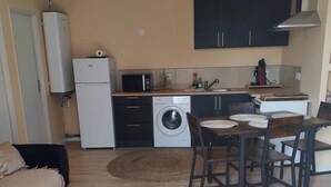 A compact living space with a kitchenette, a washing machine, a dining area with a table and chairs, and a bed. - 1-bedroom house 8 minutes from the 24H circuit (Allonnes)