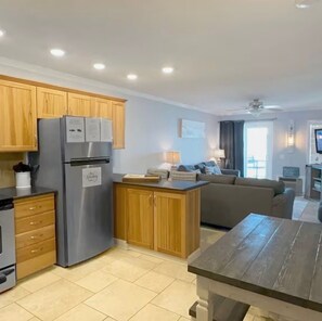 A modern kitchen with wooden cabinets, a stainless steel refrigerator, and a dining area with a table and chairs. - Oceanfront•Steps to beach•Pool view•Sleeps 6 (Myrtle beach)