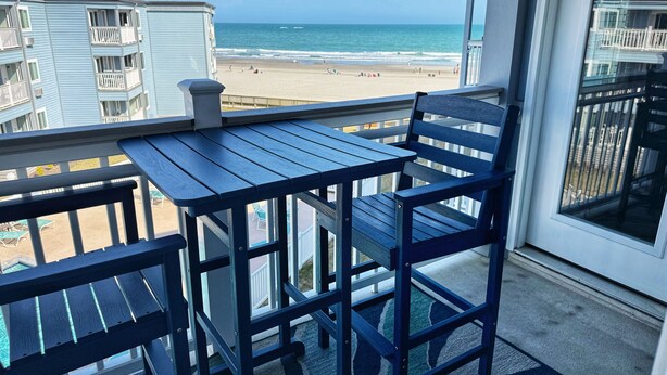 A balcony with a table and chairs overlooking a beach. - Oceanfront•Steps to beach•Pool view•Sleeps 6 (Myrtle beach)