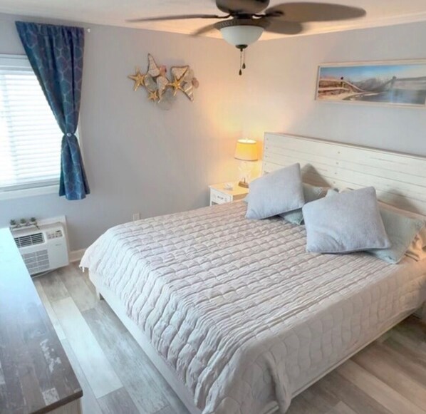 Une chambre à coucher avec un lit, un ventilateur de plafond, des œuvres d’art murales et une table de chevet avec une lampe.