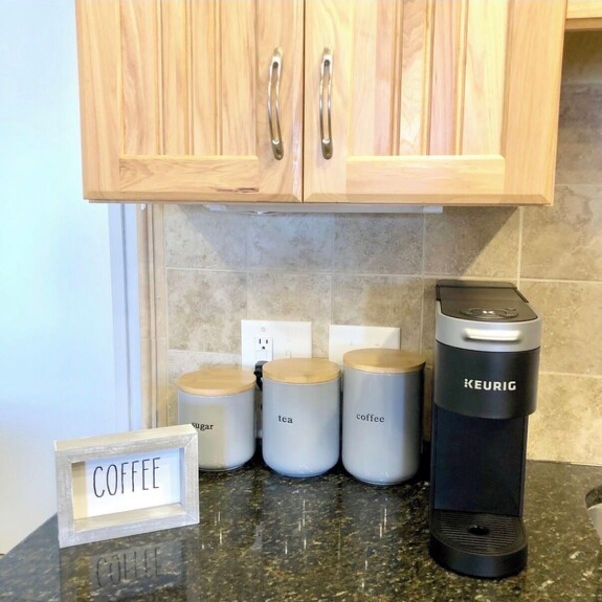 A kitchen with wooden cabinets, a coffee maker, and labeled containers for sugar, tea, and coffee.