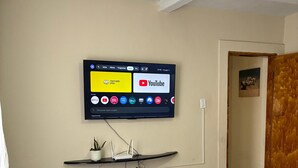 A hotel room with a bed, a mounted TV displaying various streaming services, a small shelf with a plant, and a door leading to another room. - A haven of tranquility, a house close to the center of São Lourenço. (São Lourenço)