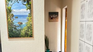 A hallway with a checkered floor, two wooden stools, a framed painting of a landscape, and a potted plant. - A haven of tranquility, a house close to the center of São Lourenço. (São Lourenço)