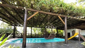 Eine Holzterrasse mit Pool, einer Hängematte und einer Rutsche.