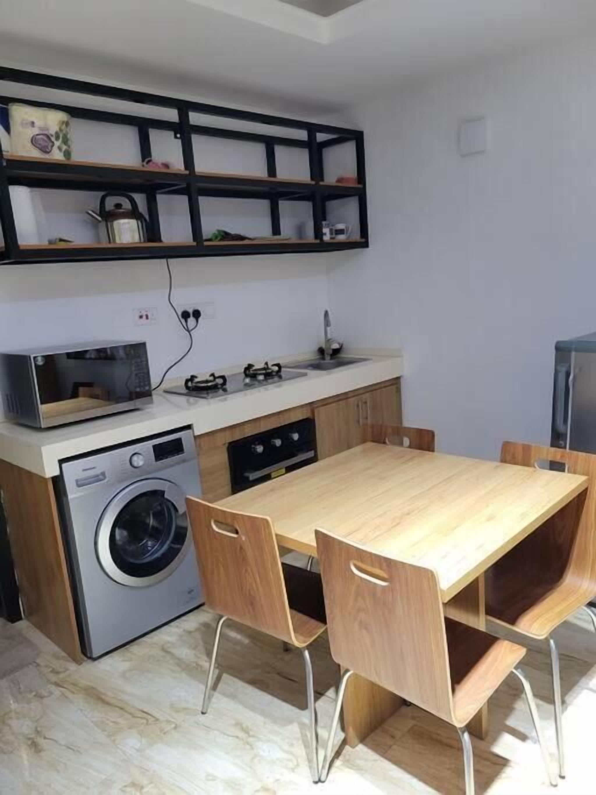 A compact kitchen with a washing machine, a microwave, a gas stove, and a wooden dining table with chairs.