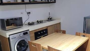 A compact kitchen with a washing machine, a microwave, a gas stove, and a wooden dining table with chairs.
