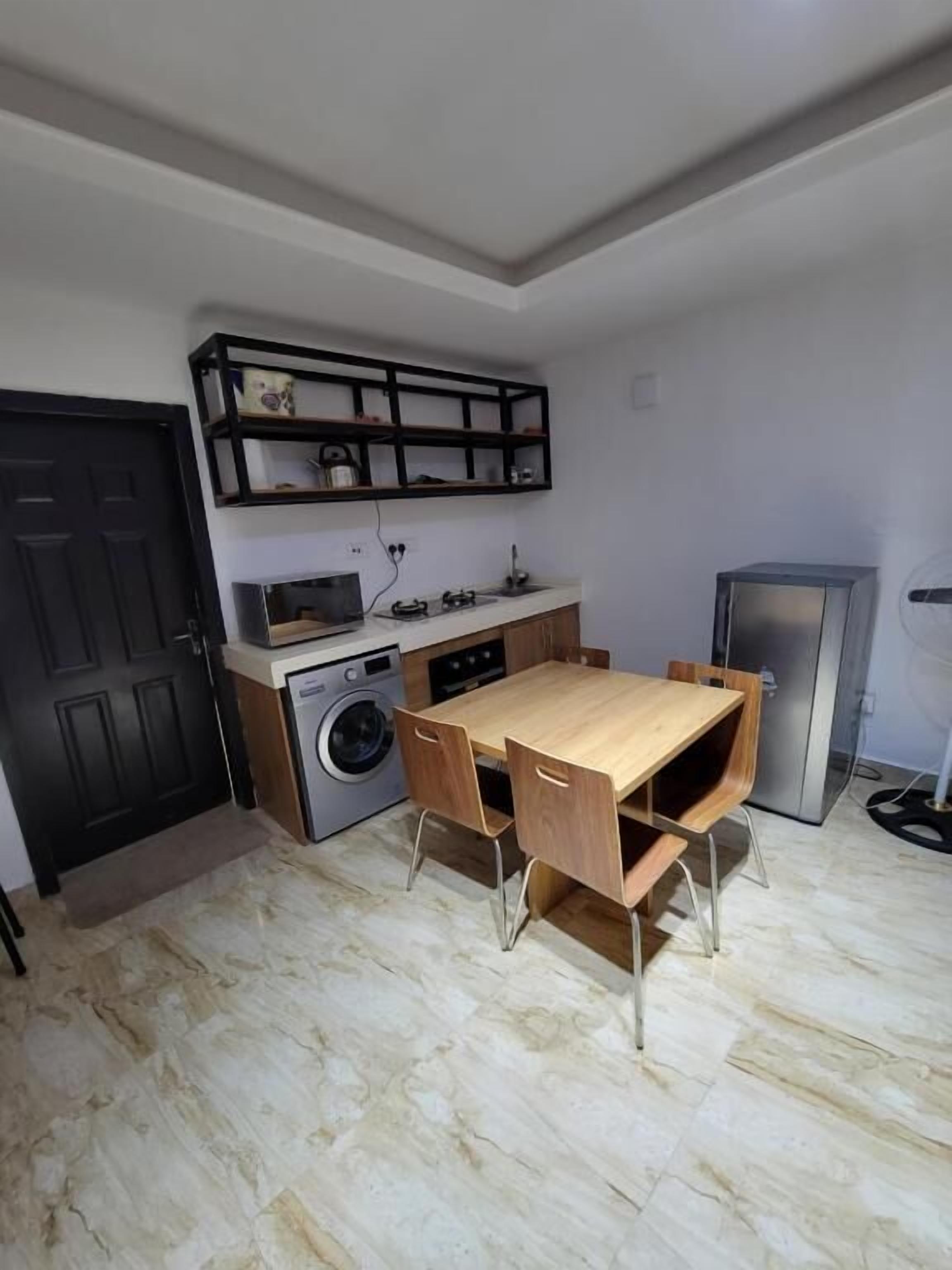 A compact kitchen with a washing machine, a dining table with chairs, a built-in oven, and a refrigerator.