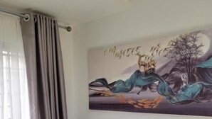 Een grijze bank in een kamer met een schilderij waarop een landschap met vogels en een boom te zien is.