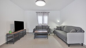 Een woonkamer met een bank, een salontafel, een tv op een meubelstuk en een lamp.