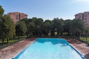 Una piscina rettangolare con acqua cristallina e blu, circondata da un bordo in mattoni e alberi.