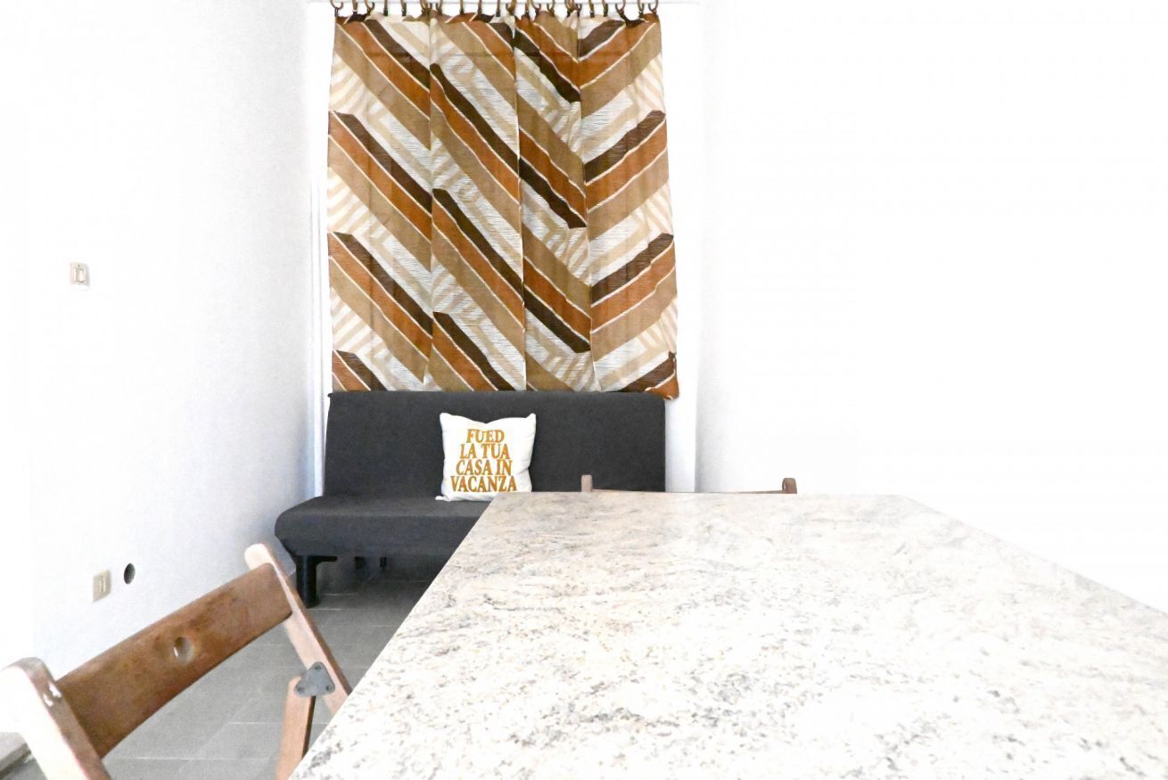 A dining area with a marble table, a black sofa with a cushion, and a chevron-patterned curtain.