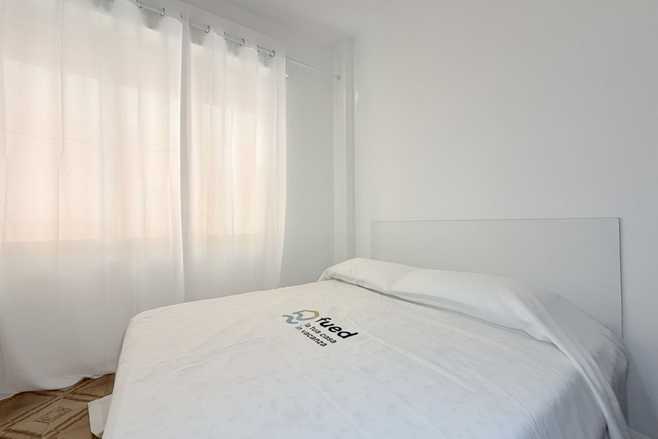 A room with a bed, a headboard, and a window with sheer curtains.