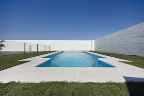 A rectangular swimming pool with a white brick wall on one side and a fence on the other.