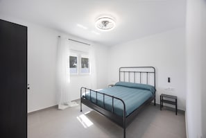 Une chambre à coucher comprenant un lit, une table de chevet, une petite table, une fenêtre avec des rideaux et un luminaire au plafond.