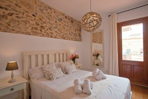A bedroom with a stone wall, a wooden bed, a bedside lamp, a mirror, and a door leading to an outdoor area. - Rustic house, ideal for families, there are 4 golf courses in 15 qm. (Artà)
