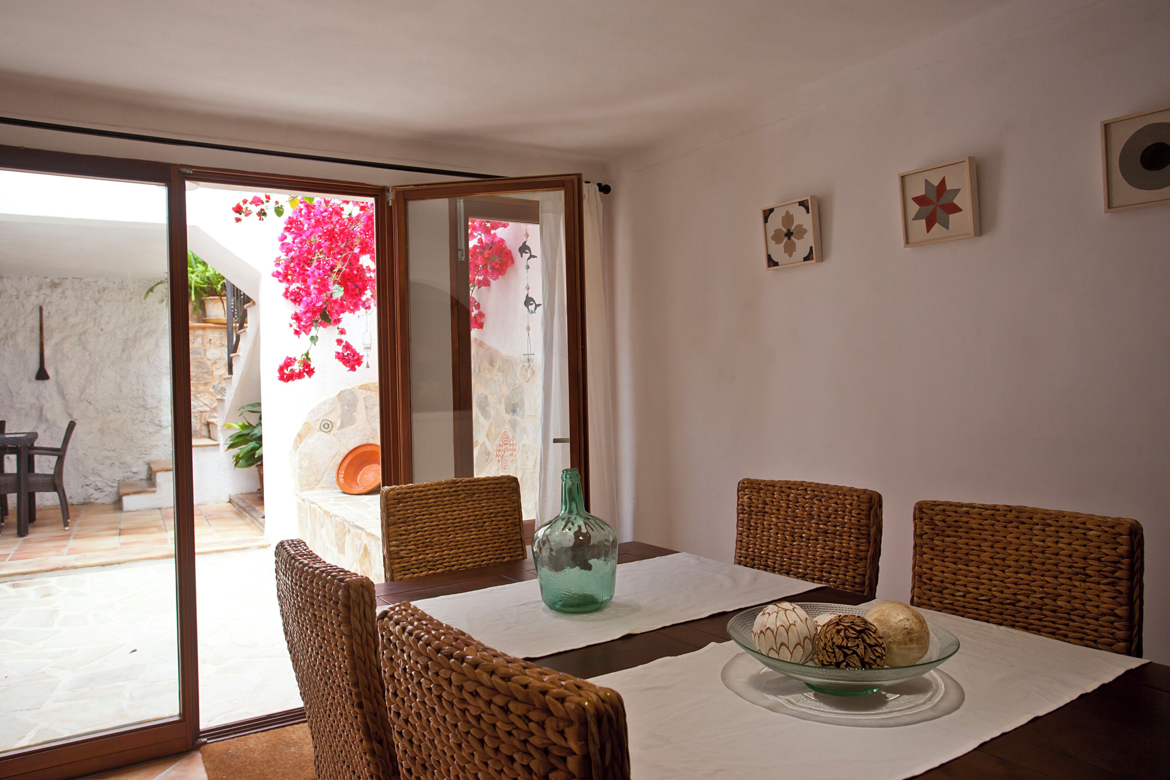 A dining area with wicker chairs, a glass table, and a bottle.
