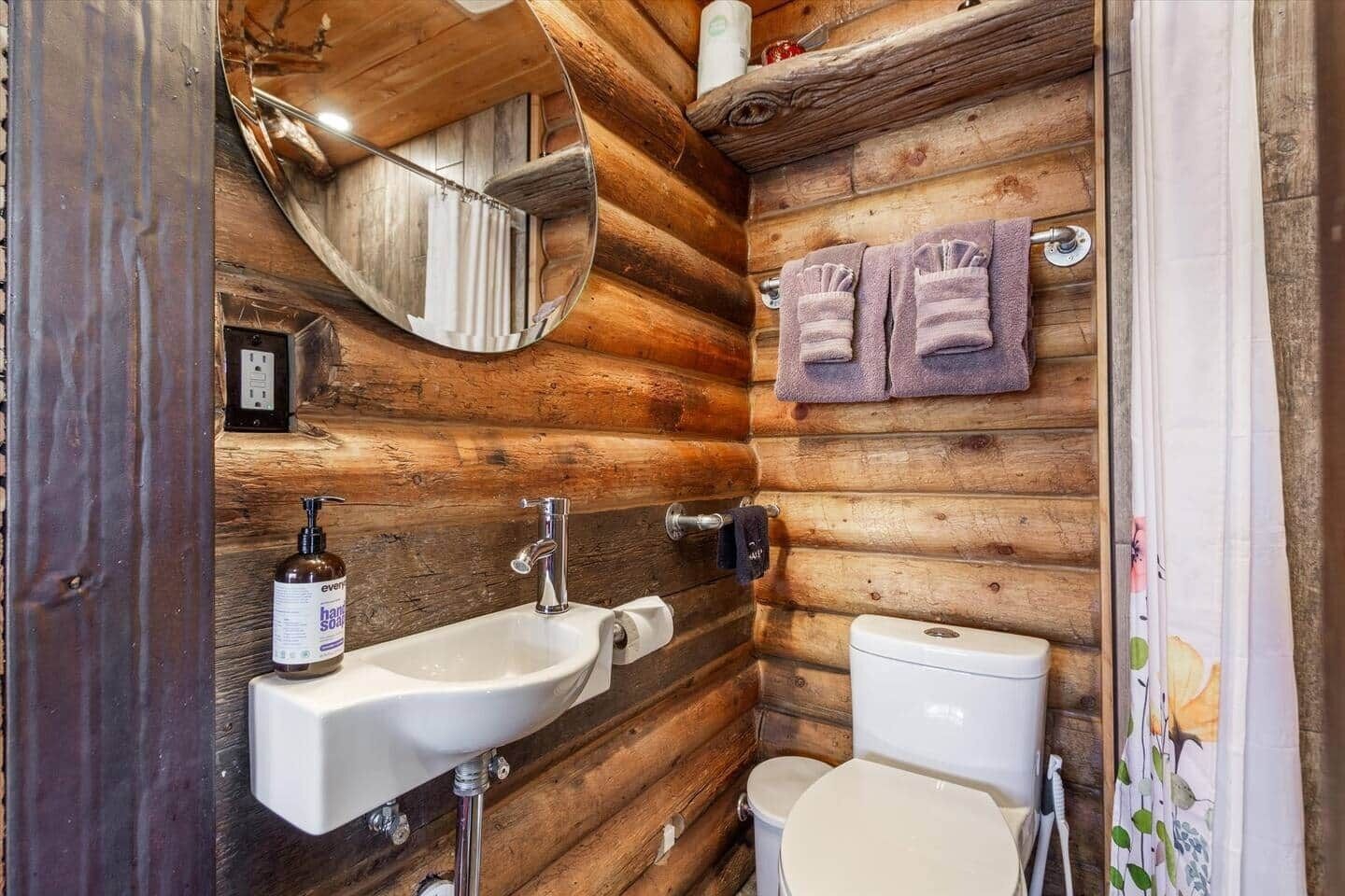 Ein Badezimmer einer Holzhütte mit Waschbecken, Toilette und Spiegel.